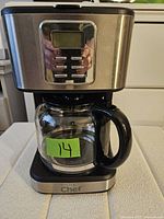 Front view of the Magic Chef coffee maker showing digital control panel, glass carafe and stainless steel and black plastic body.