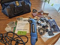 Mastercraft corded multi-crafter tool with multiple sanding, sanding pad, cutting, and scraping accessories along with the tool bag visible on wooden table.