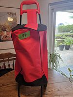 Photo of red folding shopping cart on a table inside a room near a window with a green sticky note labeled '97' on the bag