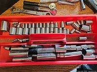 Photo showing multiple chrome sockets arranged in a red toolbox tray with additional ratchets and extensions below.
