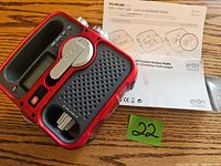 Red and black Eton SolarLink 1200 solar radio with speaker and tuning dial along with printed quick start guide manual in English and French.