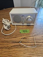 Front angle view of the white Tivoli Audio Model One radio on a wooden table showing power cord and radio controls.