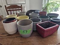 Various planters of different sizes and colors arranged on a table, including cream, gray, black, yellow, and red planters