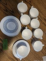 Eight Wedgwood Counterpoint cups and saucers displayed on a wooden surface, showing detailed blue floral and geometric pattern and silver edging.