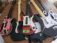 Photo showing six Wii guitar controllers on a wooden table with various designs including flame, black, and red sparkle finishes.