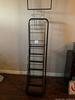 Front view of black metal display stand showing stepped wire shelves and sign holder