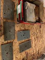 Box containing stack of steel plates with several plates laid out showing size and holes