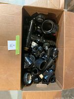 Open box showing large quantity of black plastic plumbing fittings