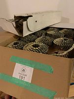 Open carton containing multiple coils of roofing nails, box label visible