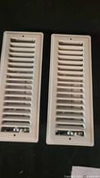 Two white rectangular louvered duct grates