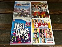 Four Nintendo Wii game cases showing Disney Sing It Pop Hits, Summer Athletics, Glee Karaoke Revolution, and Just Dance 3 arranged on a wooden surface