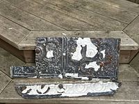 Two embossed tin ceiling trim pieces with peeling white paint and rust, laid on wooden surface. One is a corner trim and the other a straight panel.