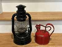 Black antique lantern with glass globe and red metal gas can with pump handle placed on wooden surface