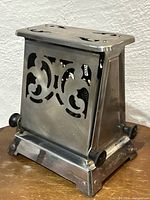 Front corner view of antique stainless steel Hotpoint toaster showing decorative cutouts and side knob.