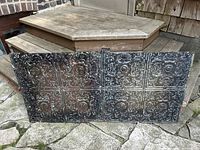 View of two embossed Victorian tin ceiling panels placed side by side, showing six decorative square sections each with floral and scroll embossed designs, black finish with weathered patina.