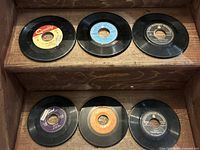 Top view of six assorted 45 RPM vinyl records with visible labels including Quality, Bluebird, Dominion, and Verve.