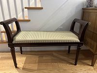 Front view of wooden bench showing sage green and cream geometric pattern upholstery with dark wood frame and curved arms.