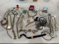 Overall collection of costume jewelry including necklaces, earrings, rings, and bracelets spread out on a white surface.
