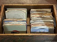 Top view showing two compartments of 45 RPM vinyl singles with paper sleeves inside a wooden crate
