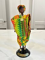 Full front view of the Ghanian Barbie doll standing on black base, displaying colorful traditional garment and head wrap.