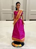 Full body view of Indian Barbie Doll showing hot pink sari with gold decorated sash and black and gold stand.