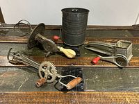 A group photo of the four vintage kitchen tools showing the flour sifter, two egg beaters, and the rotary grater all placed on a wooden surface.