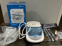 Full view of Mabis CompMist nebulizer compressor, tubing inside blue compartment, box, syringes, masks, manual spread around on table.