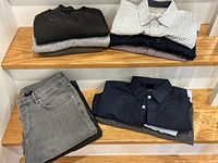 Display of folded sweaters, button-down shirts, and jeans on wooden shelves.