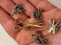 Items displayed in palm to show size and detail, showing all five pins/brooches closely grouped.