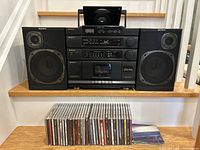 Front view of Sony CFD-454 boombox showing cassette player, CD player with lid open, radio tuner, graphic equalizer, and attached speakers. Music CDs in jewel cases arranged in front.