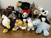 Photo showing 14 Ganz Webkinz stuffed animals arranged together on a wooden surface, featuring bears, a lion, panda, eagle, zebra, dog, bunny, horse, elephant, some with original tags.