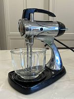 Full view of the chrome Sunbeam Mixmaster stand mixer with glass mixing bowl on black base