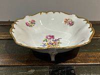 Side angled view showing scalloped rim with gold gilt trim and hand-applied floral design inside bowl and on edges. Footed base visible.