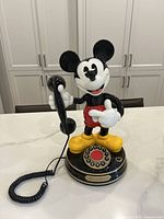 Front view of the vintage Mickey Mouse telephone on a kitchen countertop, showing Mickey holding the handset and rotary dial on the base.