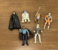 Six vintage Star Wars figures arranged on wood surface showing front of each figure, including R2-D2 and Luke Skywalker