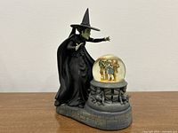 Full front view of the Wicked Witch of the West figure standing next to the snow globe with Wizard of Oz characters inside.