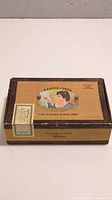 Closed view of the rectangular cardboard Garcia y Vega cigar box with vintage color graphics and brand text on top.