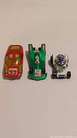Top-down view of three die-cast toy cars: red Hot Wheels racer, green Corgi Juniors Grand Prix Racer, and silver-blue Mazda RX 500 toy car.