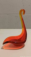 Front side profile of red and yellow handblown Murano glass swan dish on white surface against gray wall.