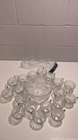 Wide view of punch bowl surrounded by 18 matching cups and ladle, showing glass etched pattern detail and overall lot contents.