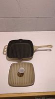 Top-down view of cream/beige enameled cast iron square grill pan and matching lid showing exterior surfaces and handles.