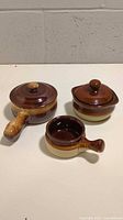 Set of three brown glazed stoneware crocks and saucepan with lids, arranged side by side