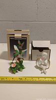 Two porcelain hummingbird statues with original boxes in the background. A measuring tape shows approximate height of 3.75 inches.