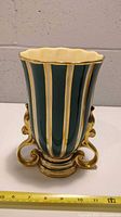 Front view of the jug with vertical dark green and gold gilt stripes and ornate curled base.