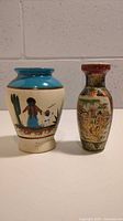Front view of both vases showing the Mexican pottery vase on the left with blue rim and folk art painting, and the GryphonWare porcelain vase on the right with colorful enamel decoration.