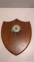 Full view of wooden shield plaque with central barometer showing minor wear and former engraving markings.
