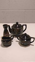Full view of the vintage Japanese 3-piece black porcelain tea set including teapot, sugar bowl, and creamer with hand-painted floral designs in pastel colors with gold accents.