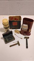 Overview of vintage shaving and grooming items including Schick Colonel electric shaver with case and box, two vintage safety razors, blue Gillette case with safety razor, Schick tin with accessories, and barbershop-style spray bottle.