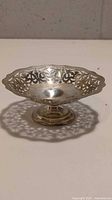 Full view of silver-plated pedestal bowl showing intricate floral cutout rim detailing and reflective interior surface