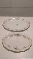 Two oval porcelain serving platters viewed from above showing pink floral pattern and gold trim